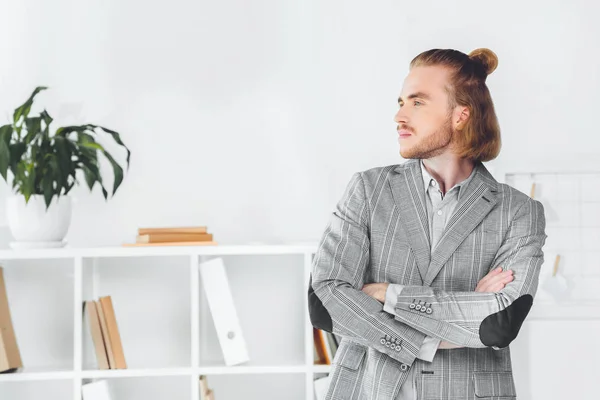 Handsome businessman standing in office with crossed arms and looking away — Stock Photo