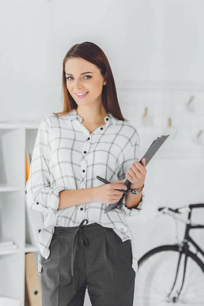 Smiling businesswoman with clipboard and pencil looking at camera — Stock Photo