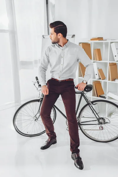 Красивий бізнесмен, спираючись на велосипед і дивлячись геть — стокове фото