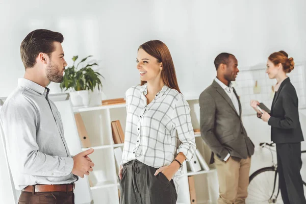 Sonrientes empresarios multiculturales de pie y hablando en la oficina - foto de stock