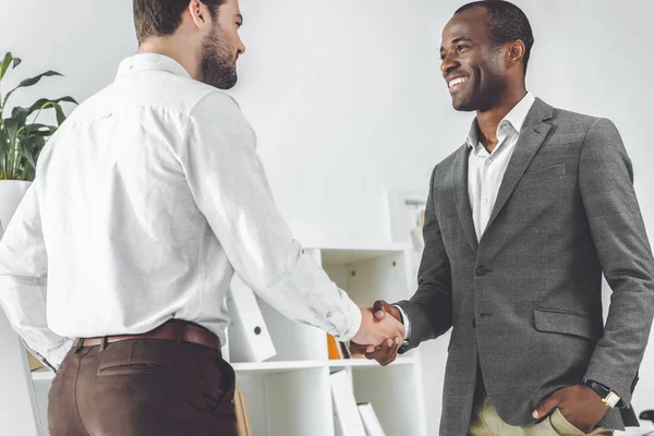 Sonrientes hombres de negocios afroamericanos y caucásicos estrechando las manos - foto de stock