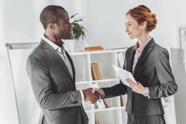 Hombre de negocios afroamericano y mujer de negocios caucásica estrechando la mano - foto de stock