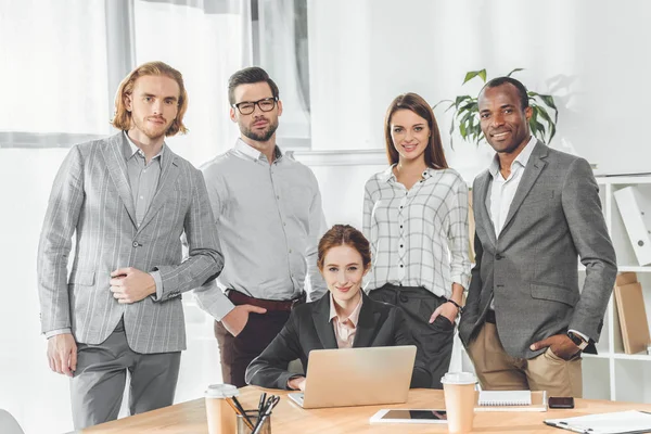 Бізнес команда стоїть проти сидячої жінки в офісному просторі — стокове фото