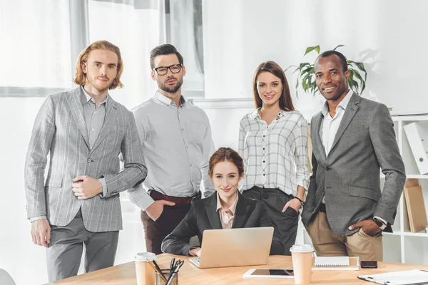 Geschäftsteam stellt sich gegen sitzende Frau im Büro — Stockfoto