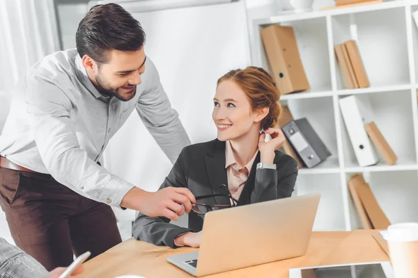 Standing man in blue shirt speaking to sitting woman against laptop on table — Stock Photo