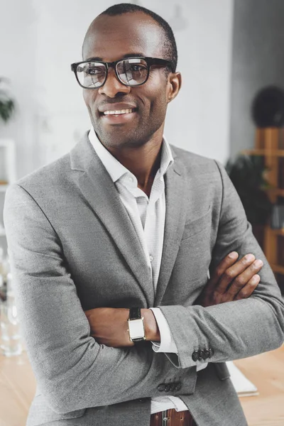 Uomo africano sorridente con le braccia incrociate guardando lo spazio ufficio — Foto stock