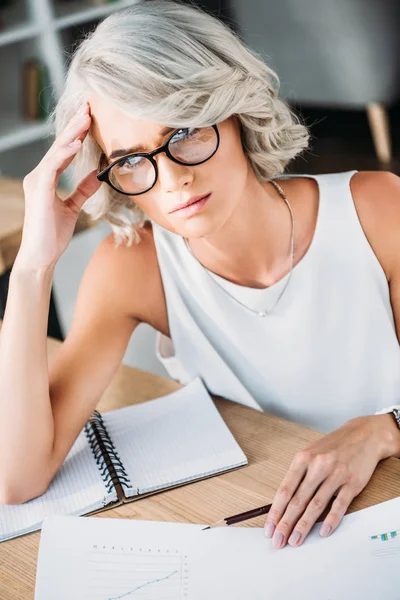 Stanco attraente giovane donna d'affari caucasica seduta a tavola in ufficio e guardando altrove — Foto stock