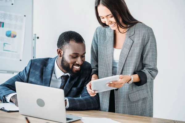 Smiling african american businessman and asian businesswoman looking at tablet in office — Stock Photo