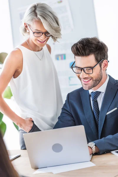 Young smiling businesspeople looking at laptop in office — Stock Photo