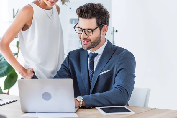 Cropped image of young smiling businesspeople looking at laptop in office — Stock Photo