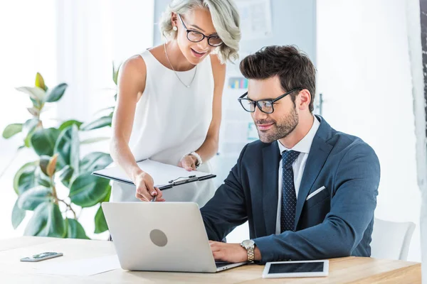 Jeunes gestionnaires souriants regardant ordinateur portable dans le bureau — Photo de stock