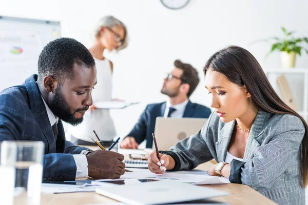 Side view of young multicultural businesspeople writing something in office — Stock Photo