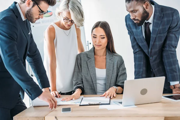 Giovani imprenditori multiculturali in piedi intorno team leader e guardando i documenti — Foto stock