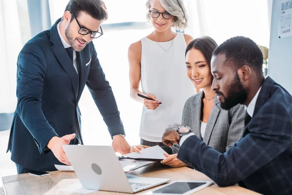 Empresários multiculturais felizes trabalhando no projeto no escritório e olhando para o laptop — Fotografia de Stock