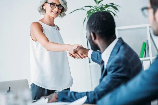 Homme d'affaires afro-américain et femme d'affaires caucasienne serrant la main au bureau — Photo de stock