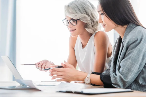 Donne d'affari multiculturali sorridenti che guardano computer portatile in ufficio — Foto stock