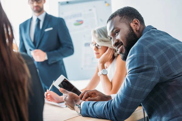 Усміхнений афроамериканський бізнесмен тримає планшет і дивиться на колегу в офісі — стокове фото