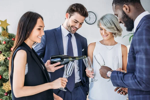 Happy businessman pouring champagne to multicultural colleagues glasses in office — Stock Photo