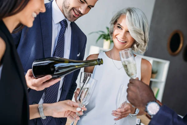 Красивый бизнесмен наливает шампанское многонациональным коллегам бокалы в офисе — стоковое фото