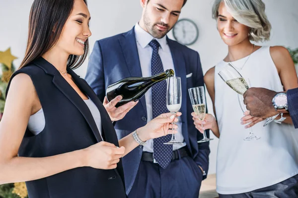 Handsome businessman pouring champagne to multicultural colleagues glasses in office — Stock Photo