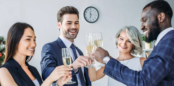 Panoramic view of multiethnic businesspeople clinking with glasses of champagne in office — Stock Photo