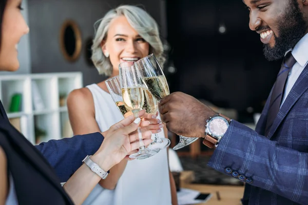 Sonrientes empresarios multiétnicos tintinean con copas de champán en la oficina - foto de stock