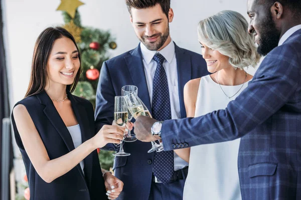 Hommes d'affaires multiethniques cliquetis avec des verres de champagne avec arbre de Noël sur le fond dans le bureau — Photo de stock