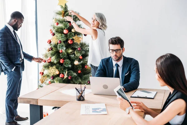 Junge multikulturelle Geschäftsleute arbeiten und schmücken Weihnachtsbaum im Büro — Stockfoto