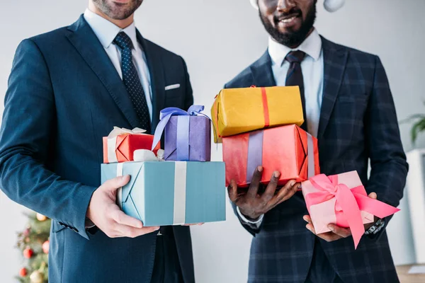 Imagen recortada de hombres de negocios multiculturales sonrientes sosteniendo cajas de regalo en la oficina - foto de stock