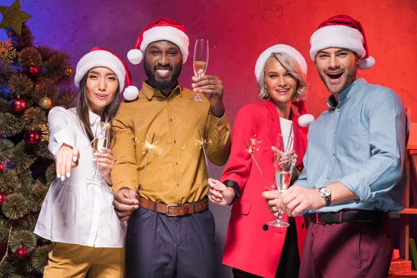 Empresarios multiétnicos celebrando chispas de Navidad y copas de champán en la fiesta corporativa de año nuevo - foto de stock