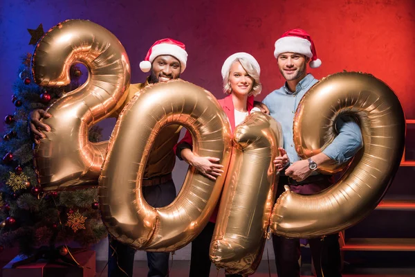 Young multiethnic businesspeople holding 2019 balloons at new year corporate party — Stock Photo