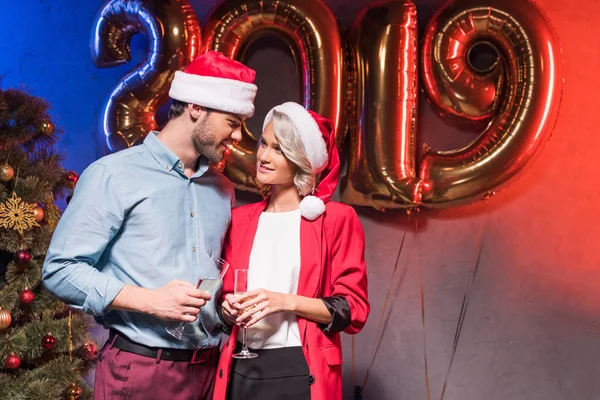 Молодые бизнесмены в шляпах Санта-Клауса смотрят друг на друга на новогодней корпоративной вечеринке — стоковое фото