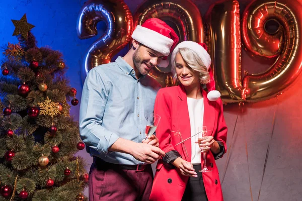 Jóvenes empresarios en sombreros de santa celebración de copas de champán y bengalas de Navidad en la fiesta corporativa de año nuevo - foto de stock