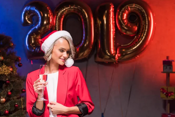 Beautiful caucasian businesswoman in santa hat holding glass of champagne at new year corporate party — Stock Photo