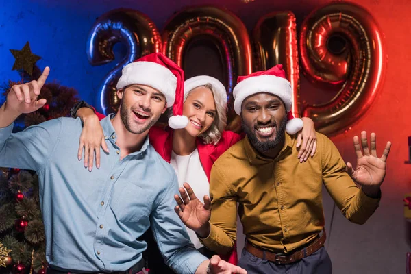 Felices empresarios multiculturales en los sombreros de santa bailando en la fiesta corporativa de año nuevo - foto de stock