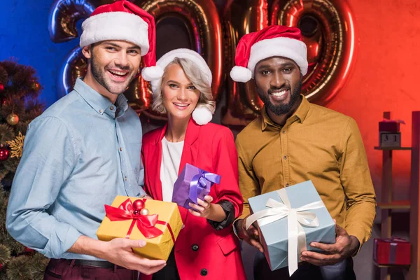 Empresários multiculturais felizes em chapéus santa segurando caixas de presente no partido corporativo ano novo — Fotografia de Stock