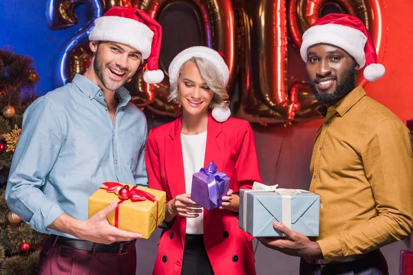 Felices empresarios multiculturales en sombreros de santa celebración de regalos en la fiesta corporativa de año nuevo - foto de stock