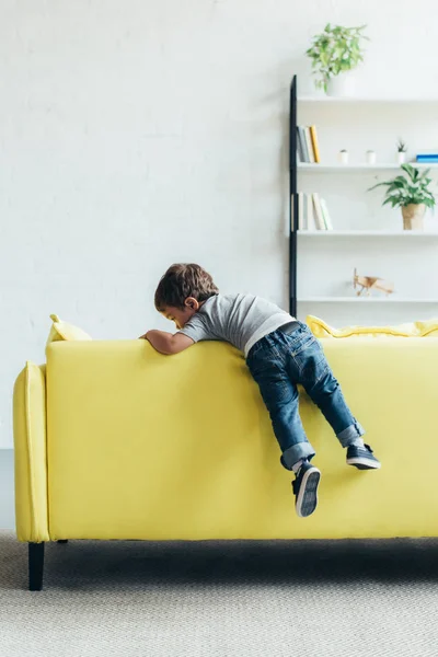 Kleiner Junge klettert zu Hause auf gelbem Sofa hoch — Stockfoto
