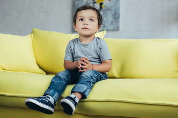 Menino adorável sentado no sofá amarelo em casa — Fotografia de Stock