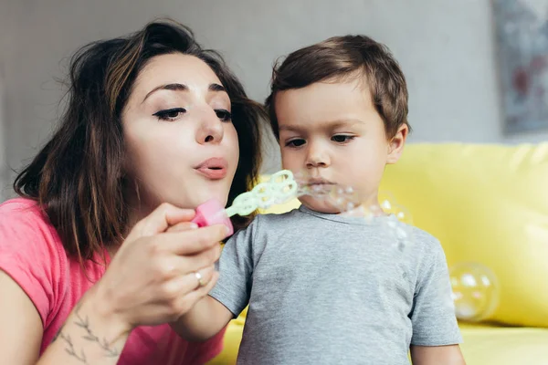 Beautiful mother and little son blowing soap bubbles together — Stock Photo