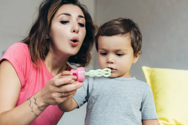 Mãe e pequeno filho soprando bolhas de sabão juntos em casa — Fotografia de Stock