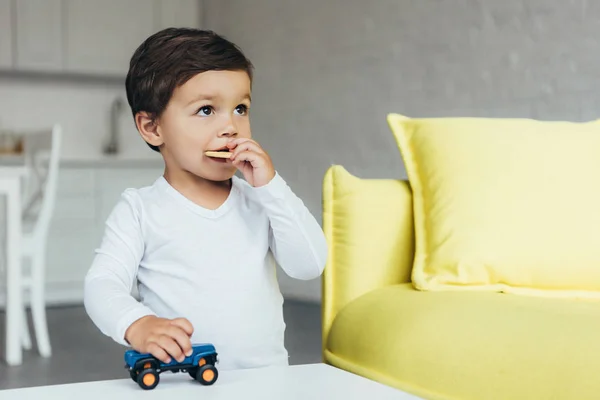 Lindo niño jugando con coche de juguete y comer galletas en casa - foto de stock