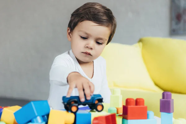 Menino adorável brincando com carro de brinquedo em blocos de construtor coloridos — Fotografia de Stock