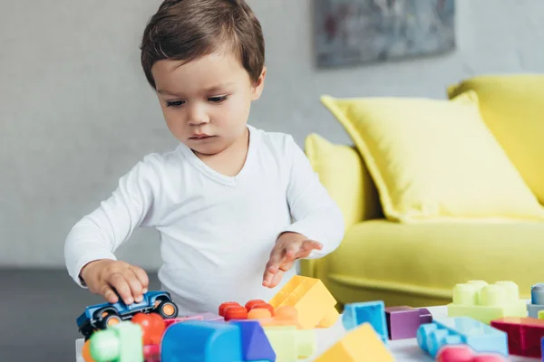 Cute kid playing with toy car and colorful constructor blocks at home — Stock Photo