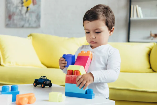 Маленький хлопчик грає з барвистими конструкторськими блоками та іграшковим автомобілем вдома — стокове фото