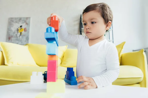 Garoto bonito brincando com blocos de construtor coloridos na mesa em casa — Fotografia de Stock