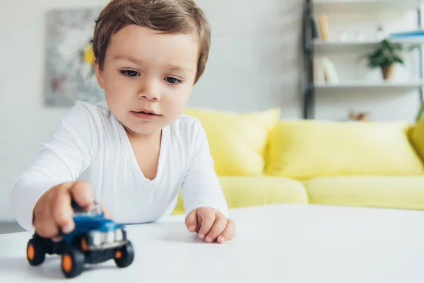 Adorable niño pequeño jugando con azul juguete coche en casa - foto de stock