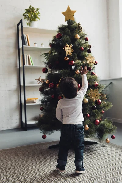 Vista trasera del niño saludando al árbol de Navidad en casa - foto de stock