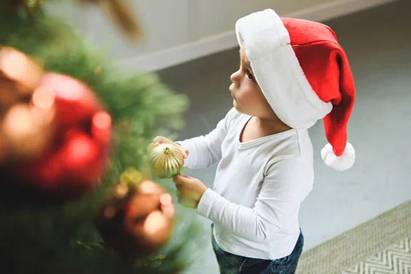 Милый мальчик в шапке Санты, украшающий рождественскую елку шариками — стоковое фото