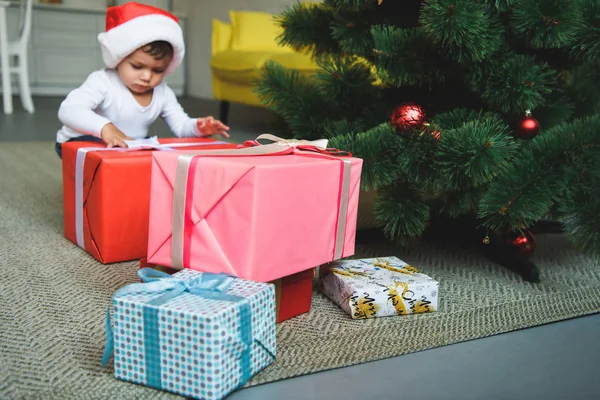 Маленький хлопчик у капелюсі Санта з подарунками біля ялинки вдома — стокове фото